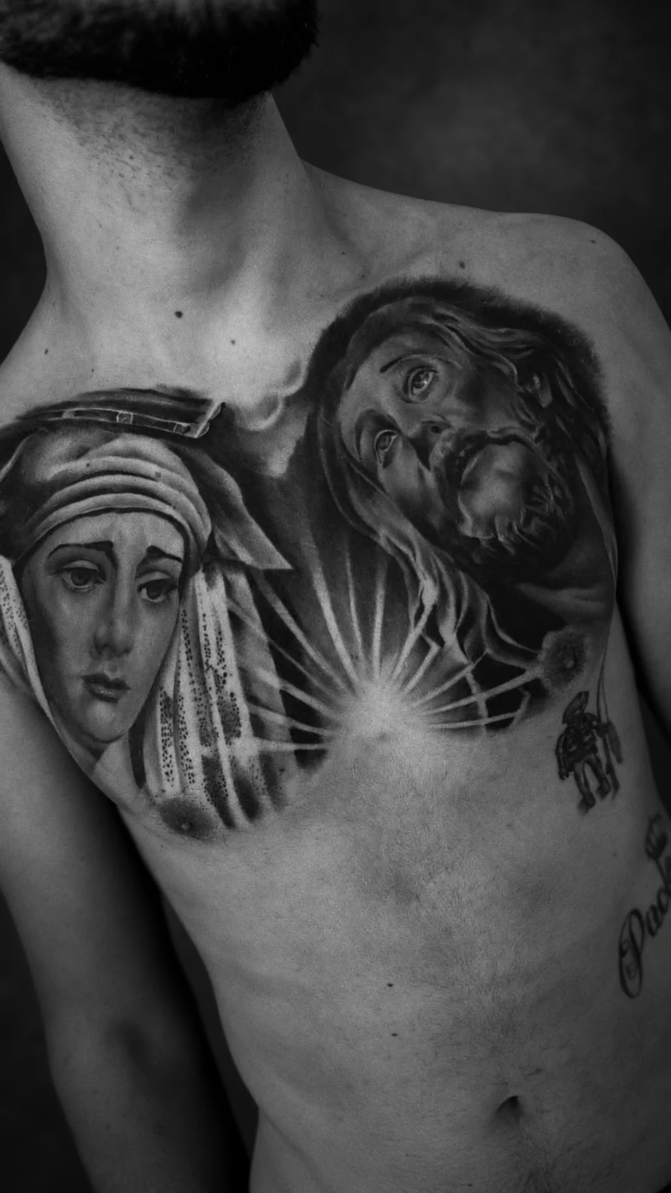 Fotografía en blanco y negro de un tatuaje en el pecho con retratos religiosos